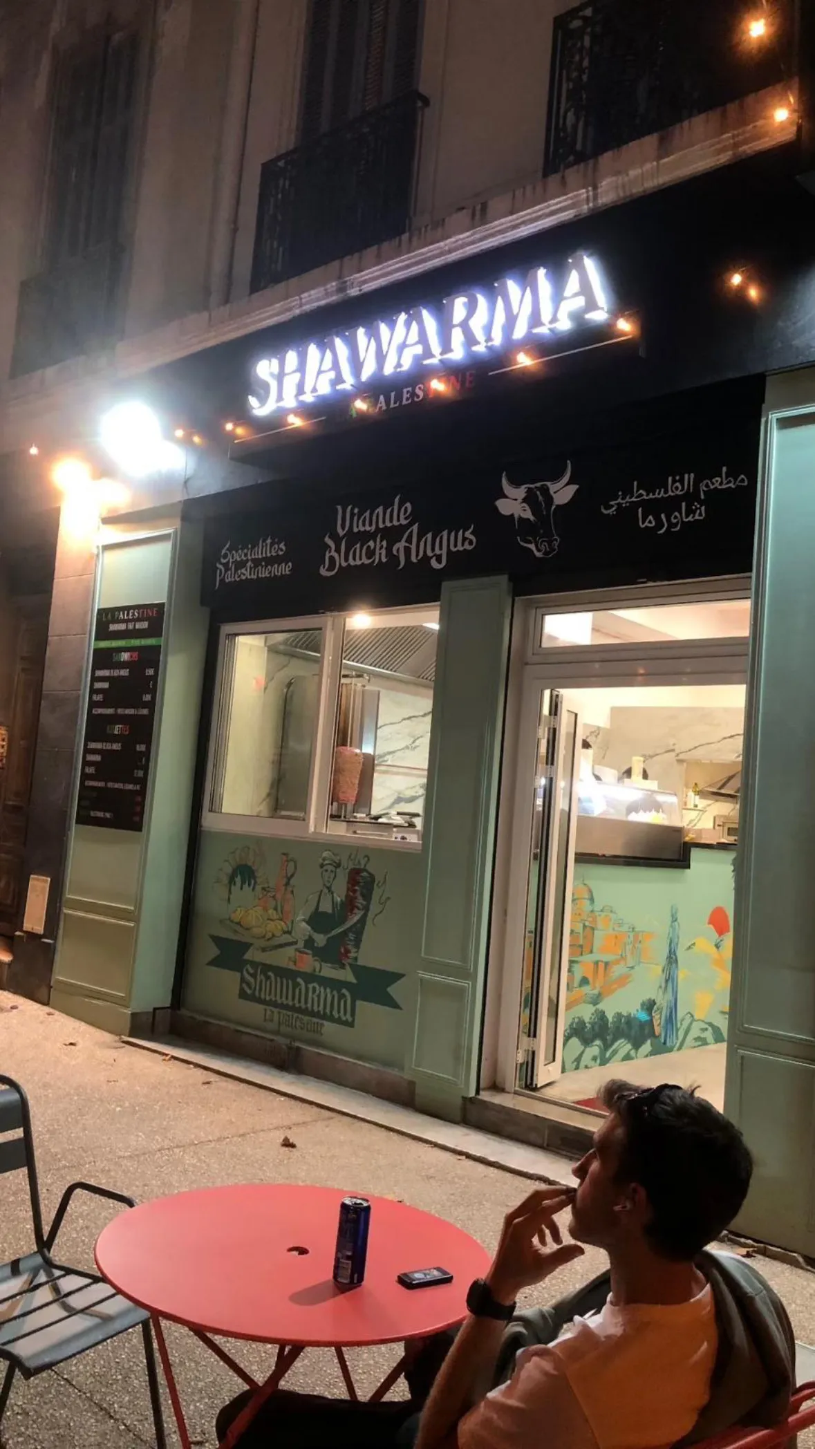 L'enseigne néon de Shawarma La Palestine allumée à la nuit tombée
